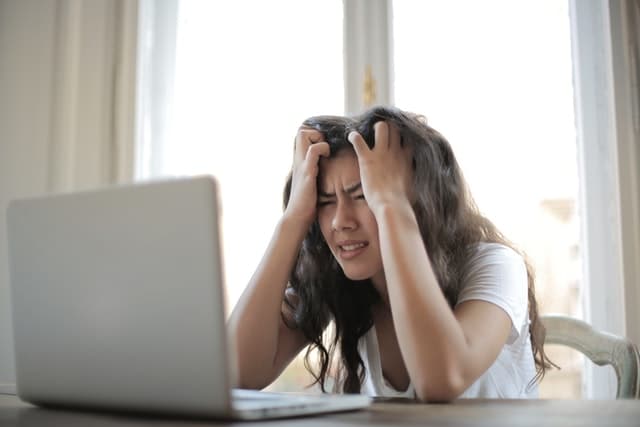 frustrated woman sitting at laptop with hands on forehead